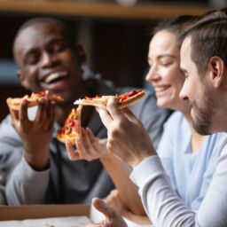 group of young adult customers smiling eating pizza